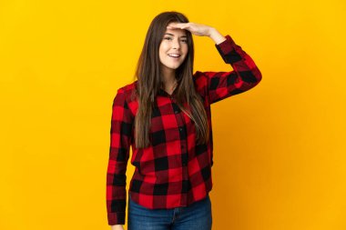 Genç Brezilyalı kız, sarı arka planda izole edilmiş. Bir şeye bakmak için uzaklara bakıyor.