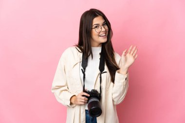 Genç fotoğrafçı Brezilyalı kız pembe arka planda izole edilmiş mutlu bir ifadeyle selamlıyor.