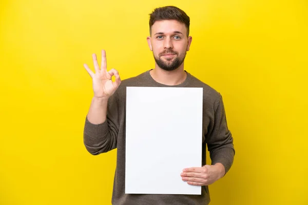 Jovem Caucasiano Isolado Fundo Amarelo Segurando Cartaz Vazio Fazendo Sinal — Fotografia de Stock