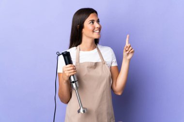 Mor arka planda izole edilmiş el blenderi kullanan Brezilyalı kadın harika bir fikre işaret ediyor.