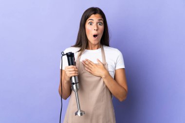 Mor arka planda izole edilmiş el blenderi kullanan Brezilyalı kadın sağa bakarken şaşırmış ve şok olmuştu.