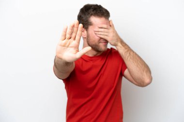 Beyaz arka planda izole edilmiş genç beyaz adam jesti durduruyor ve yüzünü kapatıyor.