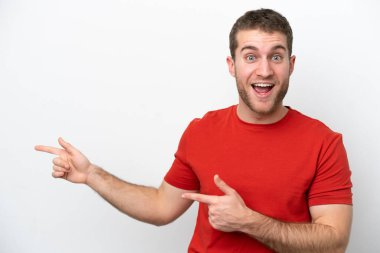 Beyaz arka planda izole edilmiş genç beyaz adam şaşırmış ve işaret ediyor.