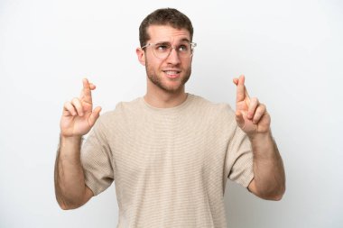 Beyaz arka planda izole olmuş genç beyaz bir adam parmaklarını çapraz yapıp en iyisini diliyor.