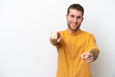 Beyaz arka planda izole edilmiş genç beyaz adam mutlu bir ifadeyle ön tarafı işaret ediyor.