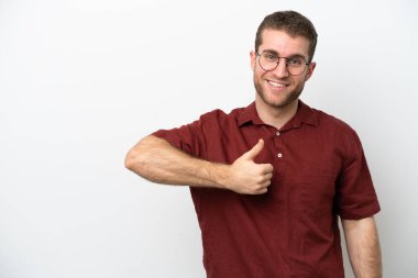 Beyaz arka planda izole edilmiş genç beyaz bir adam baş parmak hareketi yapıyor.