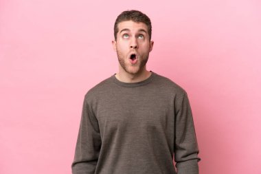 Pembe arka planda izole edilmiş genç beyaz adam yukarı bakıyor ve şaşırmış bir ifadeyle