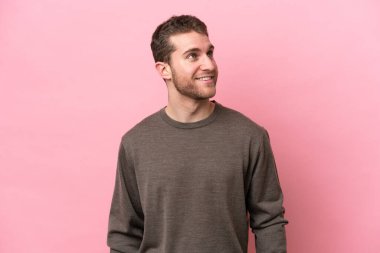 Kafkasyalı genç bir adam pembe arka planda izole edilmiş, yukarı bakarken bir fikir düşünüyor.