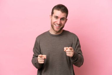 Pembe arka planda izole edilmiş genç beyaz adam şaşırmış ve ön tarafı işaret ediyor.