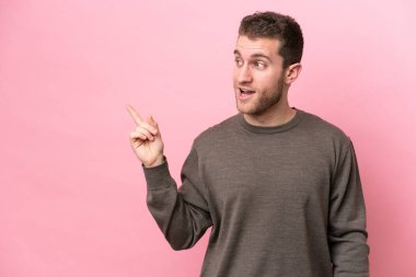 Pembe arka planda izole edilmiş genç beyaz adam çözümü bulmak için parmağını kaldırıyor.