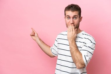 Pembe arka planda izole edilmiş genç beyaz bir adam, sürpriz bir ifadeyle işaret ederken...