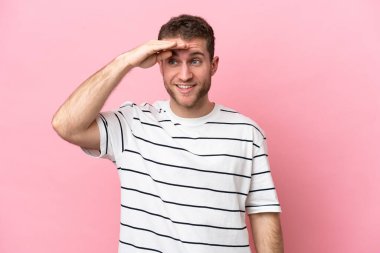 Pembe arka planda izole edilmiş genç beyaz bir adam bir şeye bakmak için çok uzaklara bakıyor.