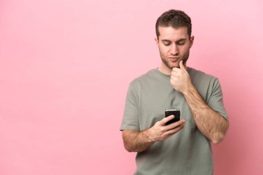 Kafkasyalı genç bir adam pembe arka planda izole edilmiş düşünüyor ve bir mesaj gönderiyor.