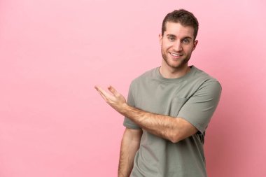 Pembe arka planda izole edilmiş genç beyaz adam gülümserken bir fikir sunuyor.