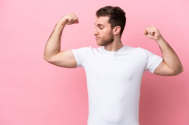 Pembe arka planda izole edilmiş genç beyaz adam güçlü bir jest yapıyor.