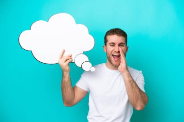 Kafkasyalı genç adam mavi arka planda izole edilmiş. Elinde düşünce balonu ve bağırış çağırış var.