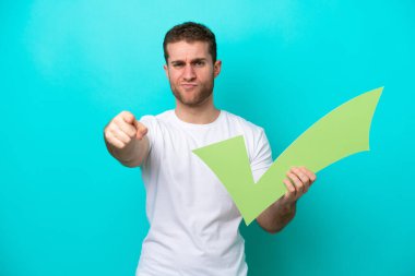 Mavi arka planda izole edilmiş genç beyaz bir adam elinde bir kontrol simgesi tutuyor ve ön tarafı işaret ediyor.