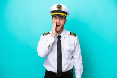 Kafkasyalı uçak pilotu mavi arka planda şaşırmış ve şok olmuş bir yüz ifadesiyle izole edilmiş.