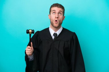 Kafkasyalı yargıç mavi arka planda izole edilmiş yukarı bakıyor ve şaşırmış bir ifadeyle