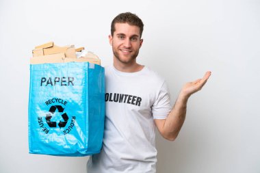Beyaz arka planda izole edilmiş bir şekilde geri dönüşüm için kağıt dolu bir torba tutan Kafkasyalı genç adam davet edildiği için ellerini yana uzatıyor.
