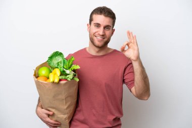 Beyaz arka planda izole edilmiş alışveriş torbası tutan beyaz bir adam parmaklarıyla tamam işareti gösteriyor.