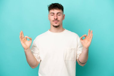 Beyaz tenli yakışıklı adam, mavi arka planda Zen pozuyla izole edilmiş.