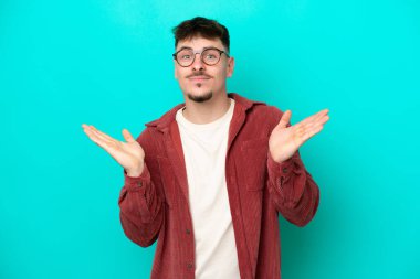 Mavi arka planda izole edilmiş beyaz, yakışıklı genç bir adam şüpheli hareketlerde bulunuyor.