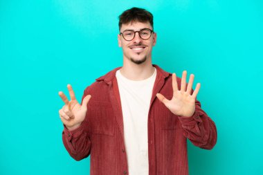 Beyaz tenli yakışıklı adam mavi arka planda izole edilmiş, parmaklarıyla sekizi sayıyor.