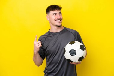 Sarı arka planda izole edilmiş genç futbolcu harika bir fikre işaret ediyor.