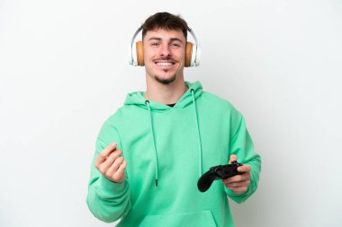 Beyaz arka planda izole edilmiş bir bilgisayar oyunu kontrolörüyle oynayan yakışıklı genç adam para hareketi yapıyor.