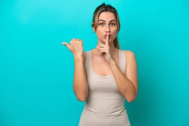 Mavi arka planda izole edilmiş genç, beyaz bir kadın. Yan tarafı işaret ediyor ve sessiz hareketler yapıyor.