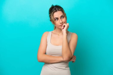 Mavi arka planda soyutlanmış, yorgun ve sıkılmış bir ifadeyle genç beyaz kadın.