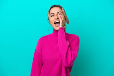 Mavi arka planda izole edilmiş genç beyaz kadın ağzı açık bağırıyor.