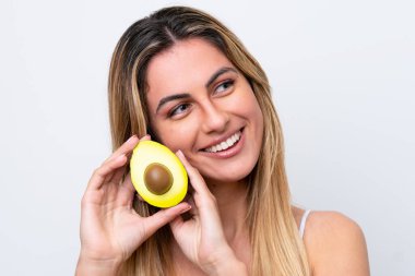 Beyaz arka planda izole edilmiş beyaz bir kadın elinde bir avokado tutarken gülümsüyor. Portreyi kapat