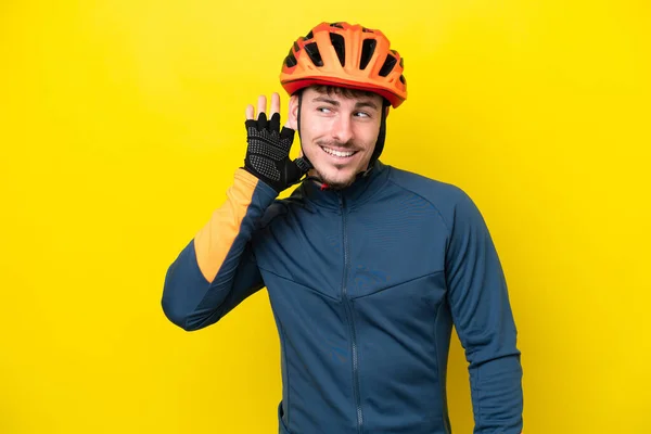 Joven Ciclista Caucásico Aislado Sobre Fondo Amarillo Escuchando Algo Poniendo —  Fotos de Stock