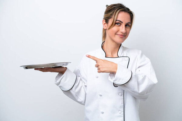 Young chef woman with tray isolated on white background pointing to the side to present a product