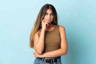 Kafkasyalı genç bir kadın mavi arka planda izole edilmiş. Şüpheleri ve düşünceleri var.