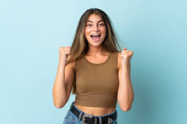 Mavi arka planda izole edilmiş genç beyaz kadın galibiyeti kutluyor.