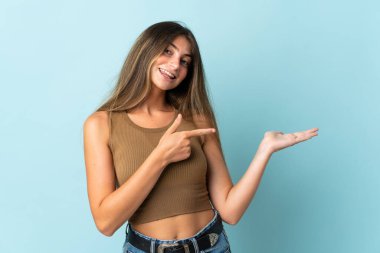 Mavi arka planda izole edilmiş genç beyaz kadın bir ilan vermek için avucunun içinde hayali bir fotokopi makinesi tutuyor.