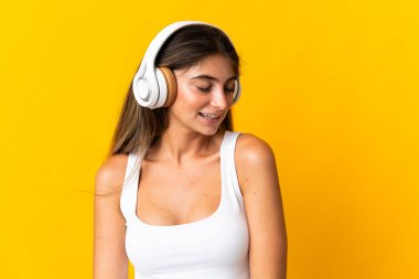 Sarı arka planda izole edilmiş genç beyaz kadın müzik dinliyor.