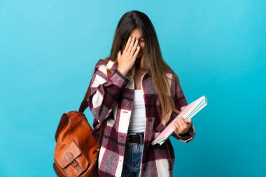 Genç bayan öğrenci mavi arka planda izole edilmiş, yorgun ve hasta bir ifadeyle.
