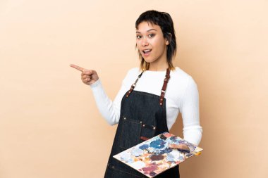 Arka planda palet tutan genç bir sanatçı şaşırmış ve parmağıyla kenarı işaret ediyor.