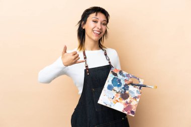 Arkaplanda palet tutan genç bir sanatçı telefon jesti yapıyor.