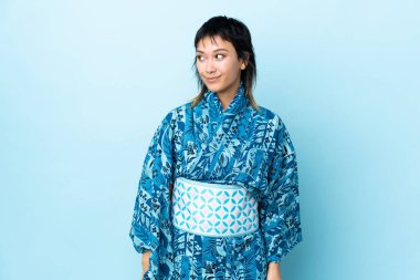 İzole edilmiş mavi arka planda kimono giyen genç bir kadın.