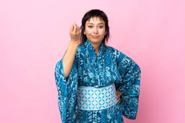 İzole edilmiş mavi arka planda kimono giyen genç bir kadın İtalyan jesti yapıyor.