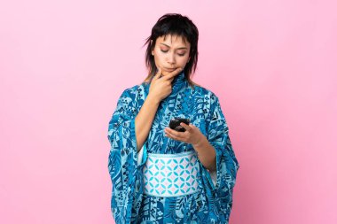 Kimono giyen genç bir kadın izole edilmiş mavi arka planda düşünüyor ve bir mesaj gönderiyor.