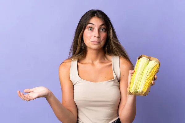 Young Woman Holding Corn Isolated Purple Background Making Doubts Gesture — Stock Photo, Image