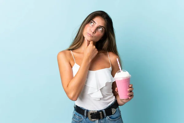 Ung Kvinna Med Jordgubbsmjölkshake Isolerad Blå Bakgrund Med Tvivel — Stockfoto