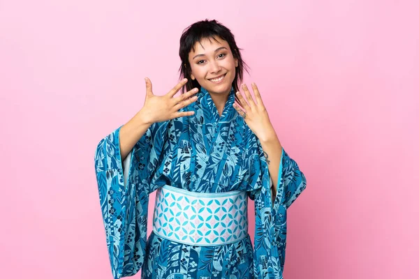 İzole edilmiş mavi arka planda kimono giyen genç bir kadın parmaklarıyla dokuz kişi sayıyor.