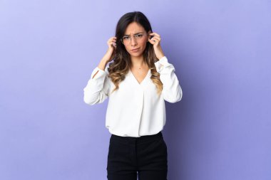 Mor arka planda izole edilmiş genç beyaz kadın hayal kırıklığına uğramış ve kulaklarını kapatmış.